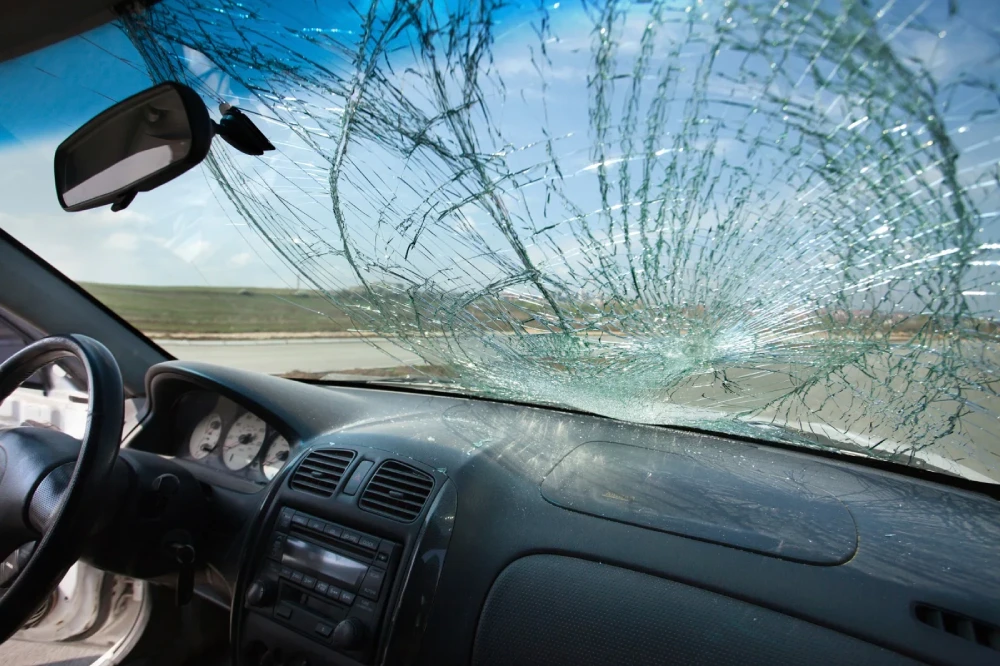 Interior view of a car with a severely shattered windshield showing extensive impact cracks, highlighting the need for professional windshield replacement for safe driving.