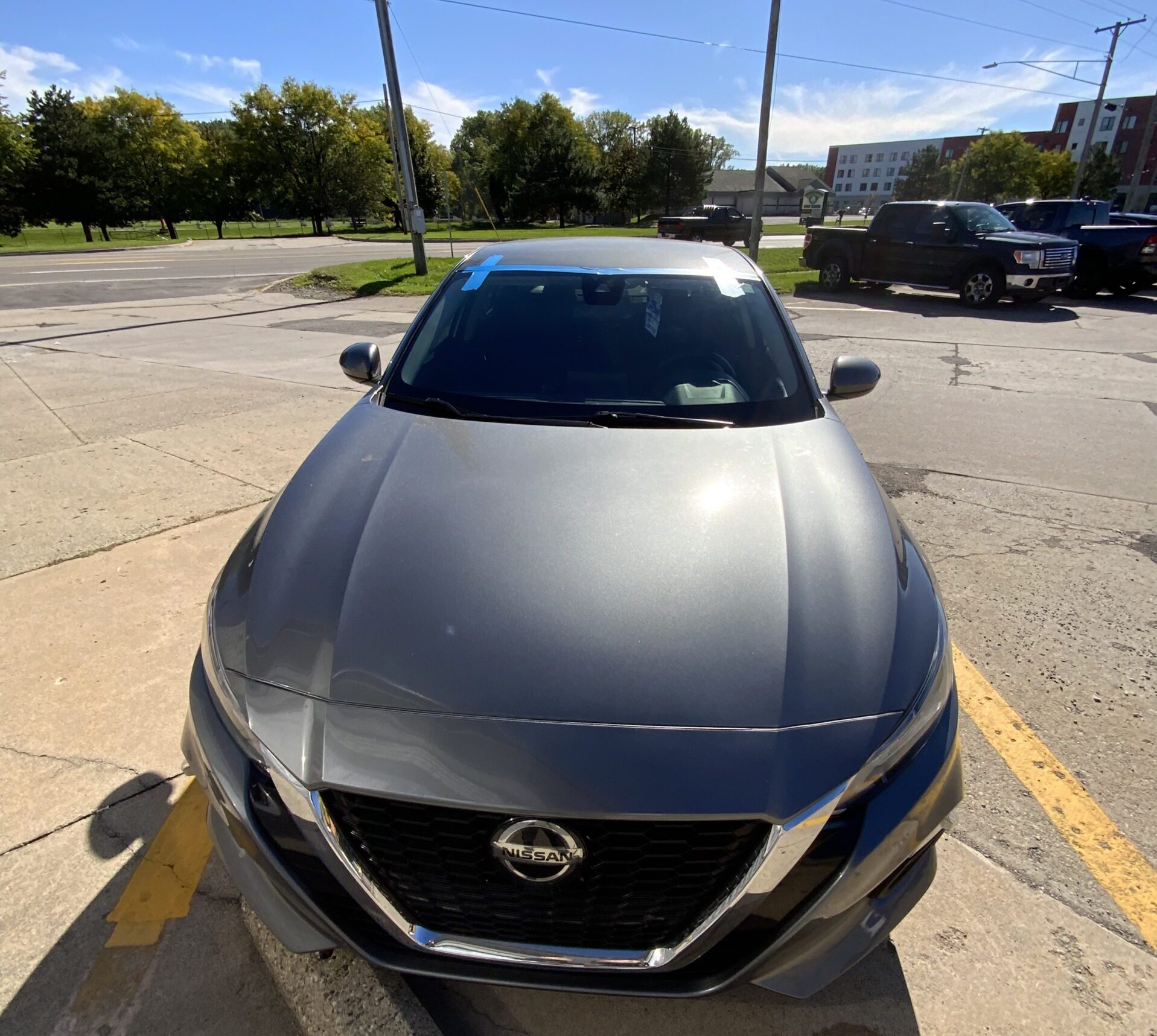 Black car parked outdoors in a parking lot in Fenton, Michigan, showing the windshield and exterior exposed to direct sunlight and outdoor weather conditions.