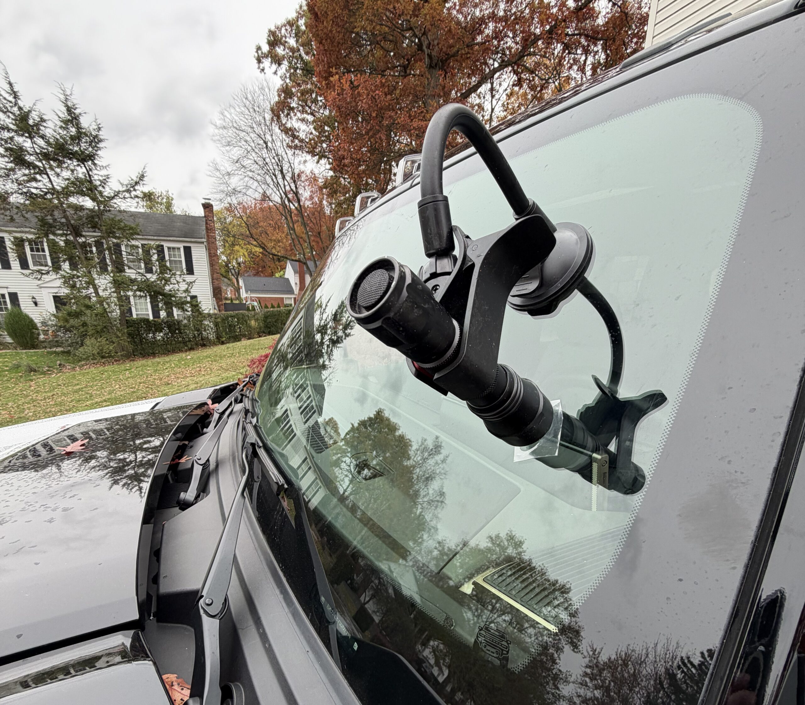 Windshield of a dark vehicle with a suction-cup gooseneck mount holding a flashlight over the repair area, mobile windshield repair by Save On Auto Glass on a residential street