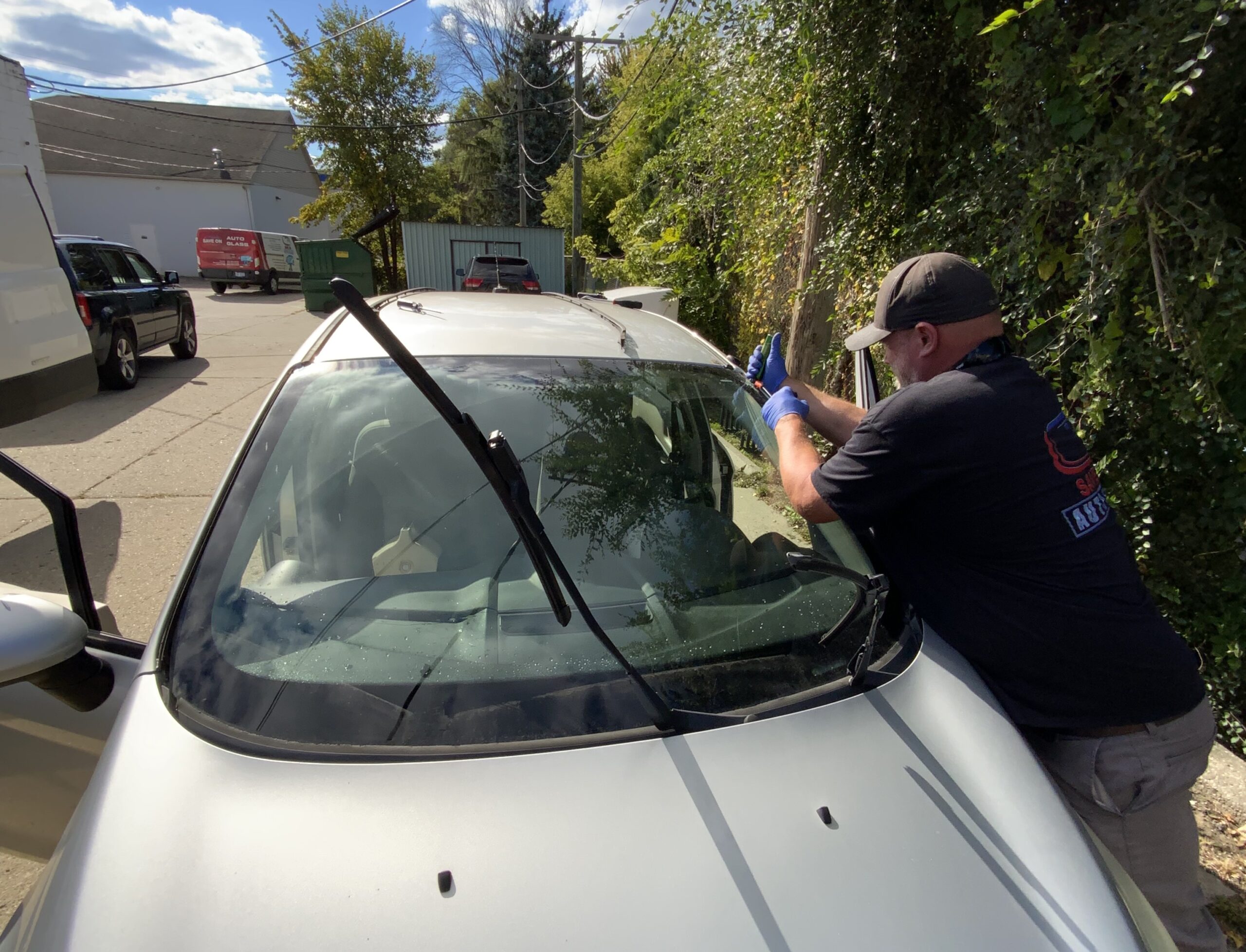 Technician wearing blue gloves working on a car windshield outdoors during mobile auto glass service