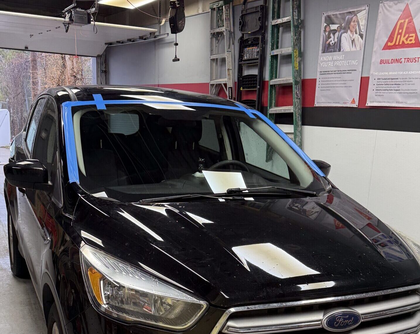 Black Ford with blue tape around a newly installed windshield inside the Save On Auto Glass shop