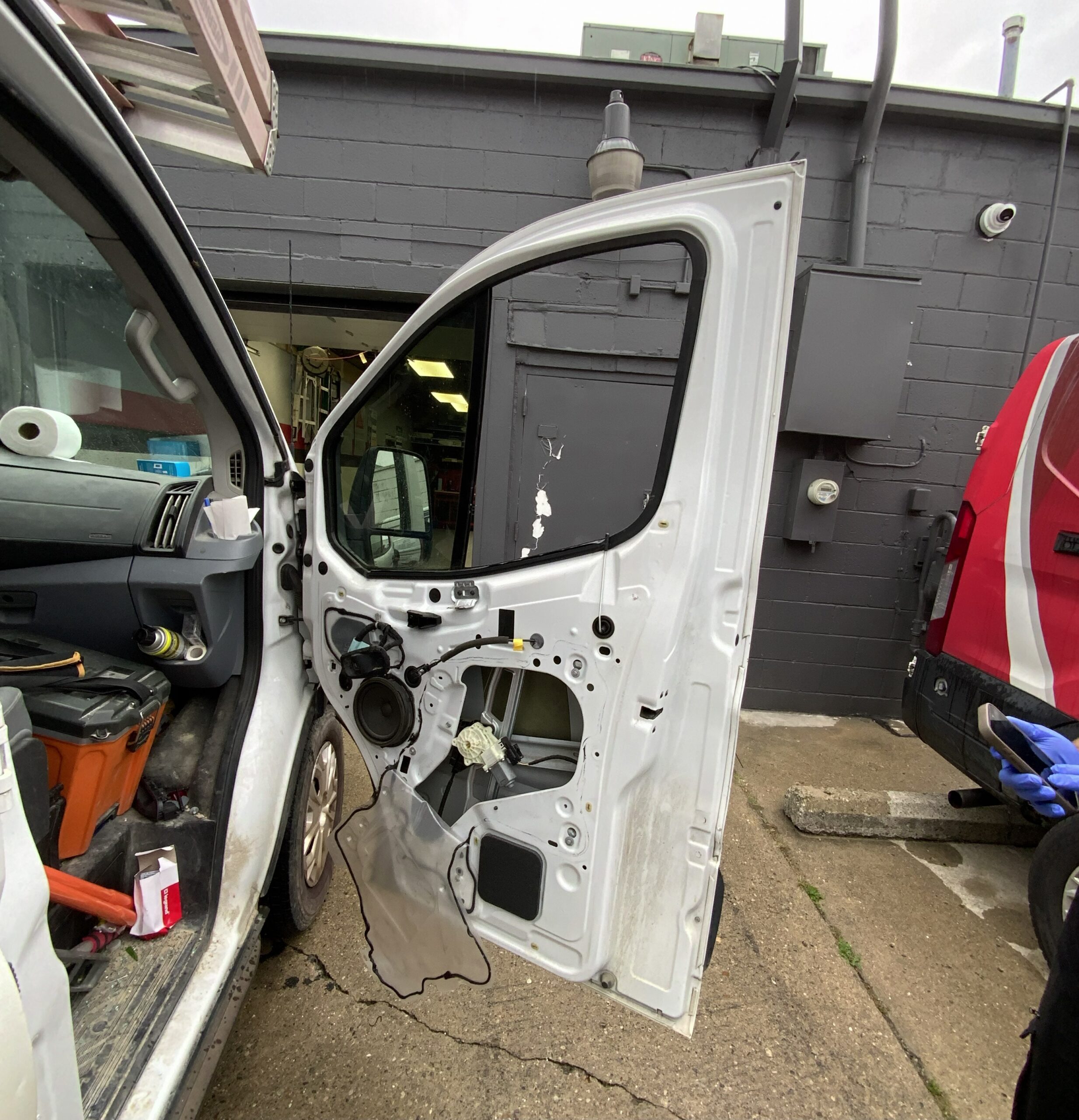 Technician repairing the power window inside the driver door of a white van with the door panel removed