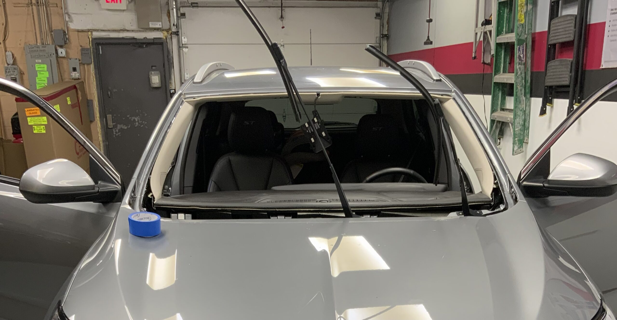 Silver vehicle with the old windshield removed and the empty frame exposed, windshield being replaced by Save On Auto Glass in the shop