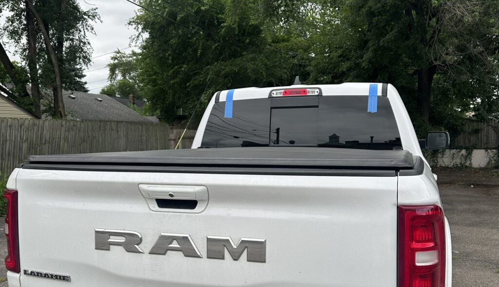 White Ram Laramie pickup truck with back glass replaced by Save On Auto Glass, blue tape still on the top corners of the new glass