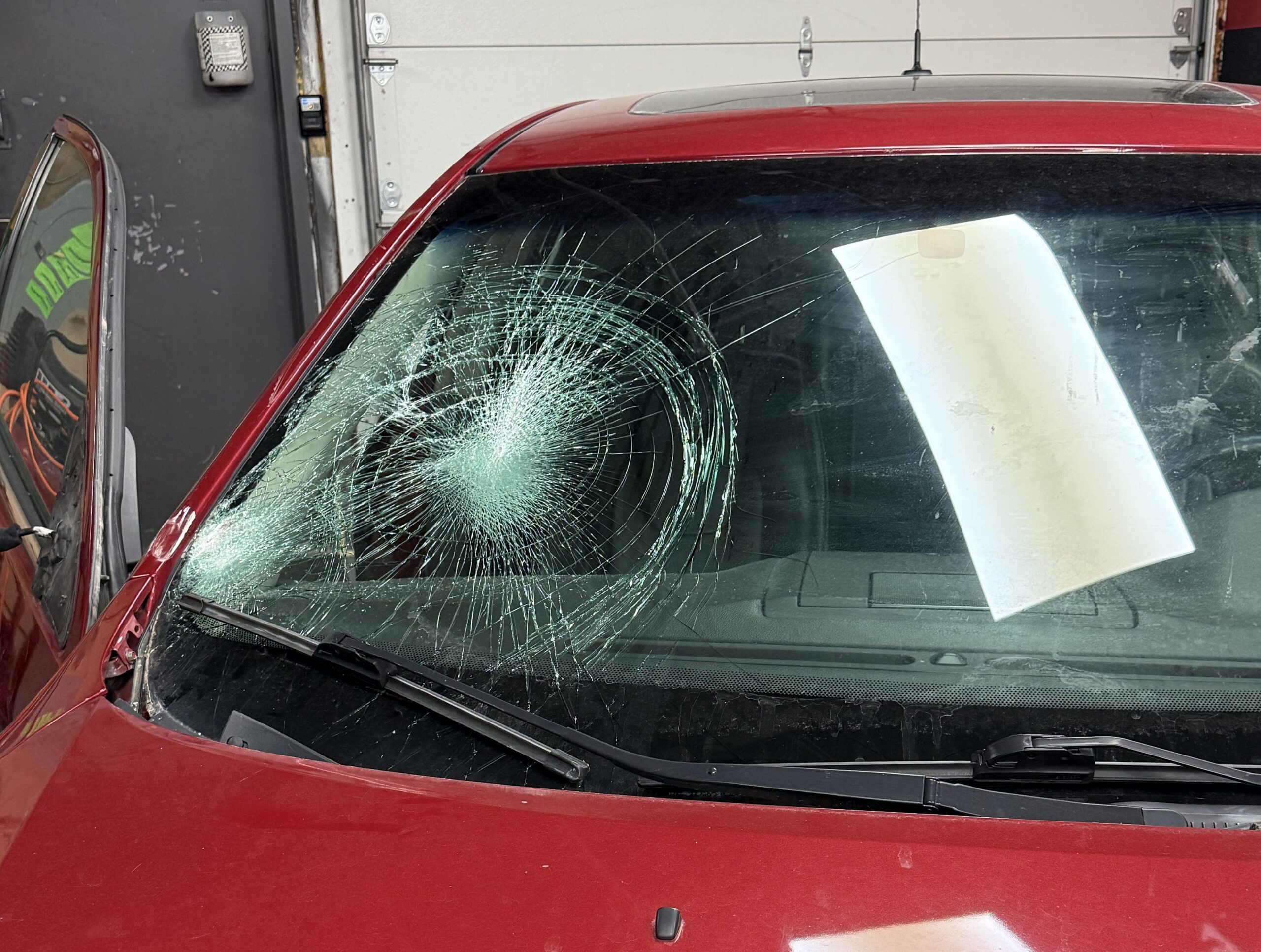 Red car with severely cracked windshield at Save On Auto Glass