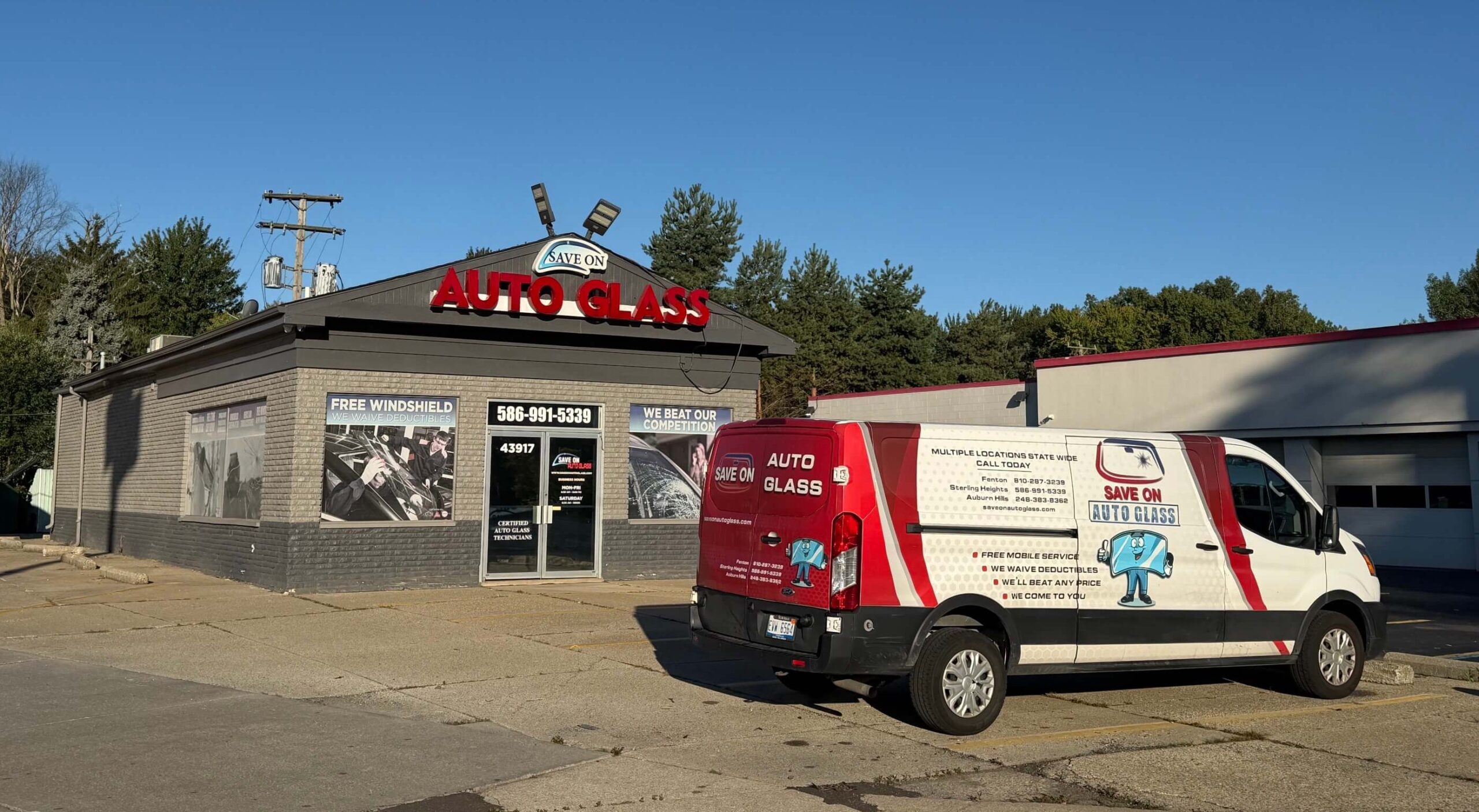 Exterior of a Save On Auto Glass shop with a red-and-white service van parked in front under a clear blue sky.