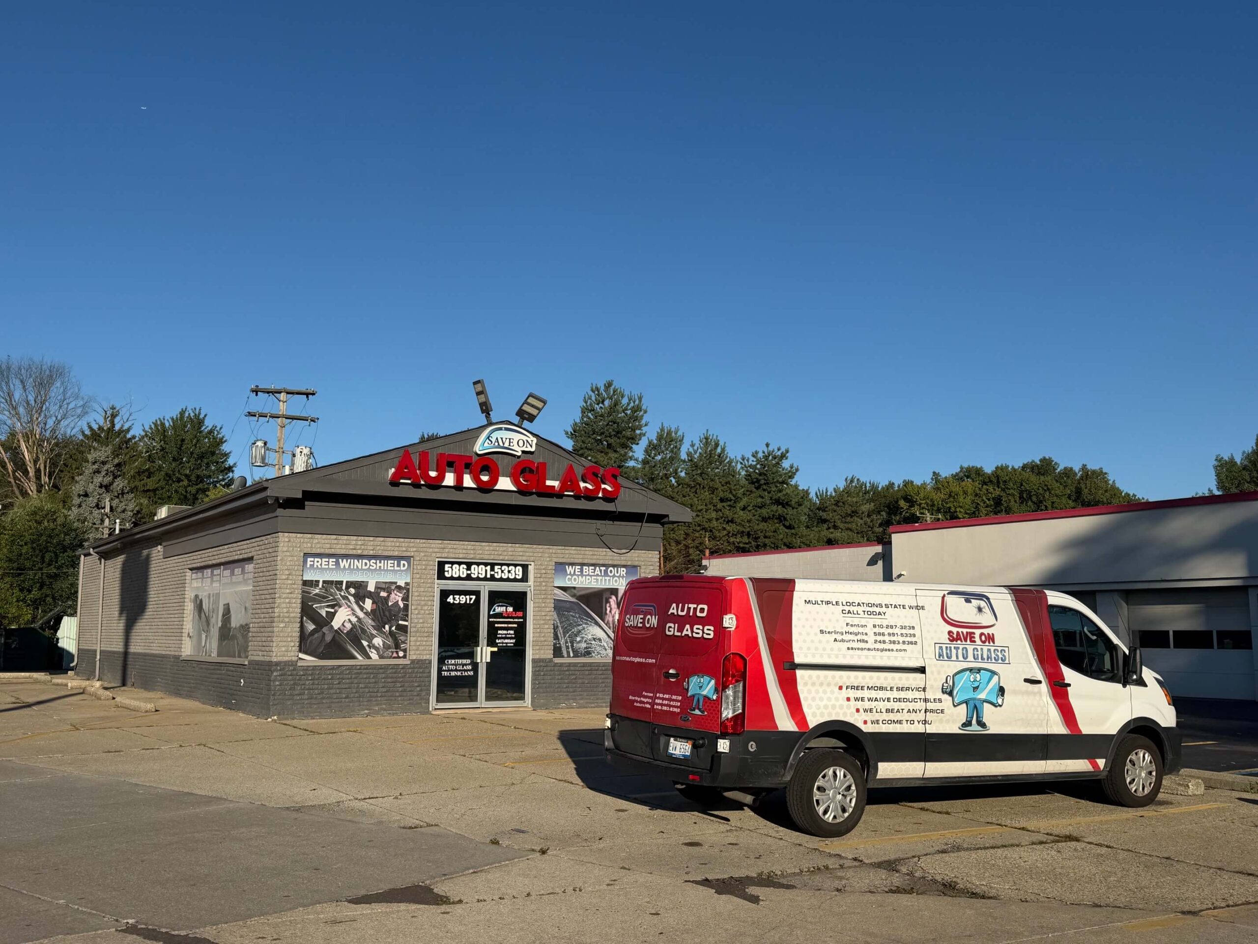 Exterior of a Save On Auto Glass shop with a red-and-white service van parked in front under a clear blue sky.