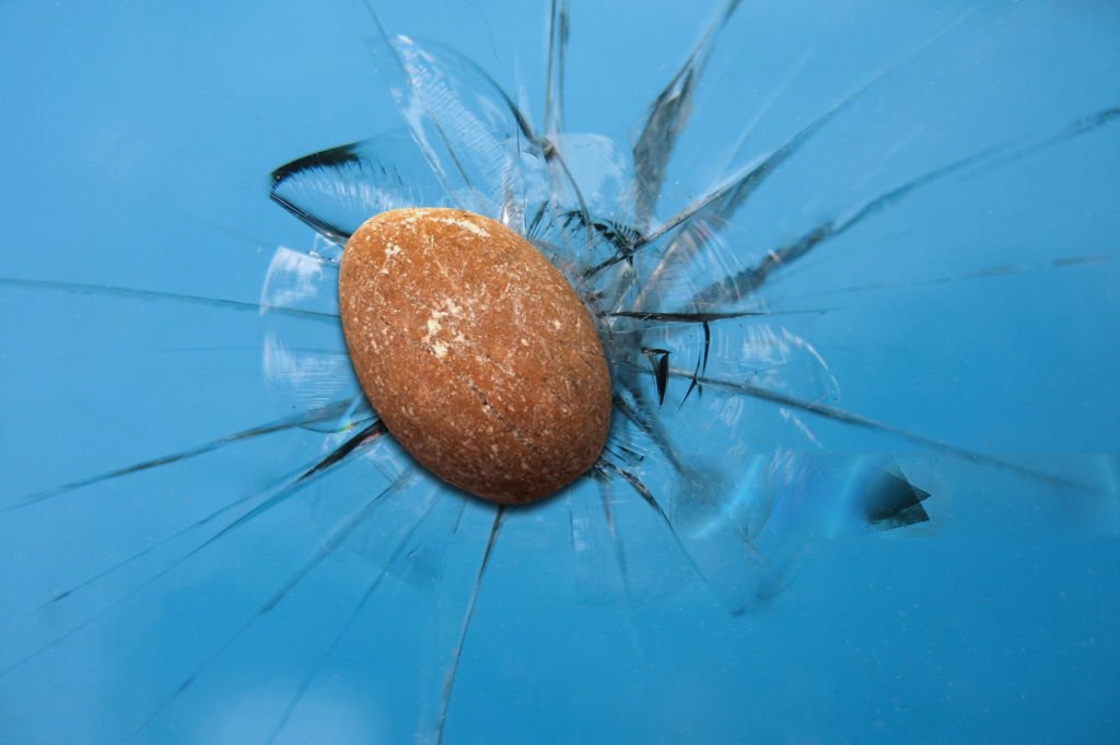 The thrown stone hits and shatters the window glass