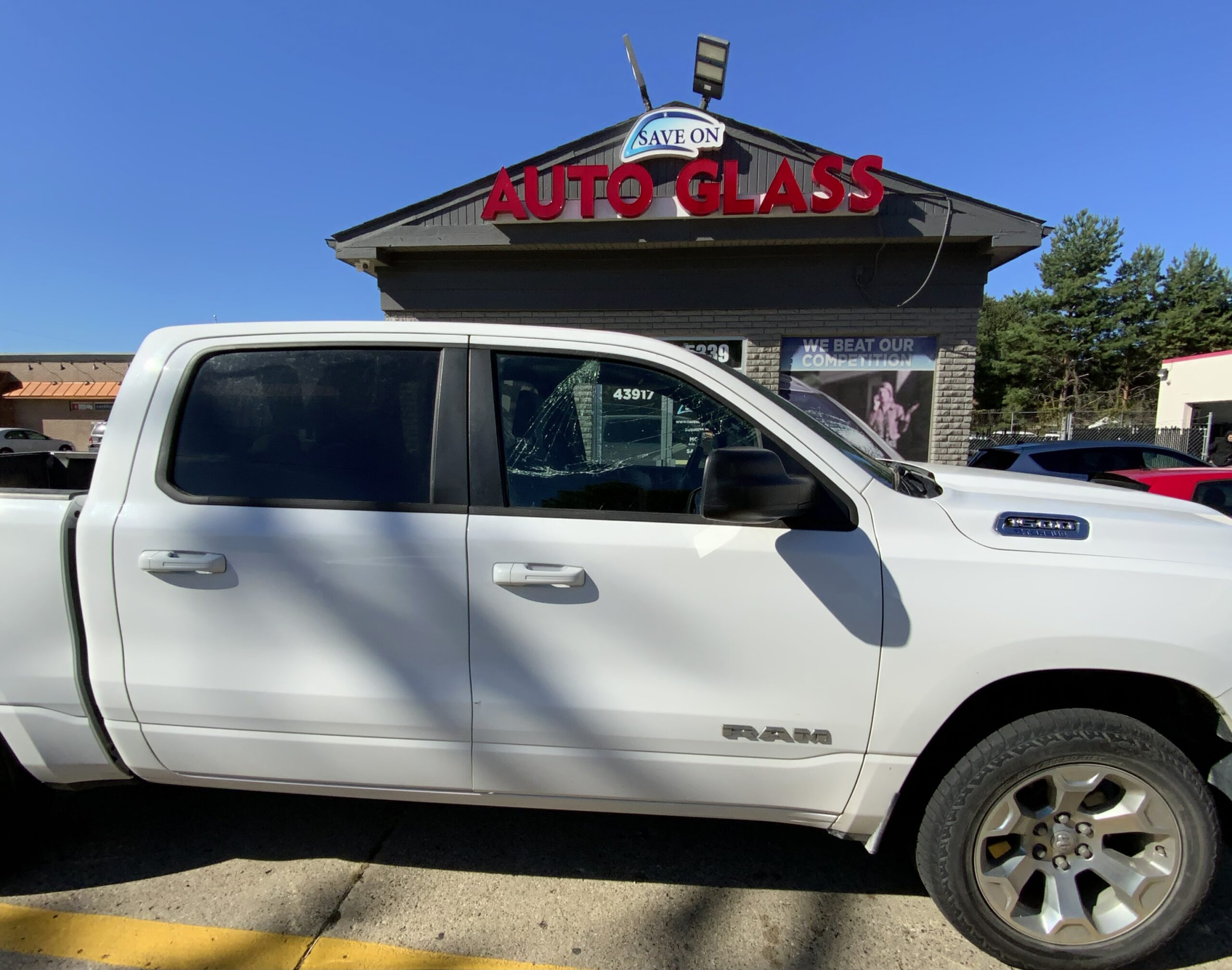 White Ram crew cab pickup truck parked in front of the Save On Auto Glass shop, side view