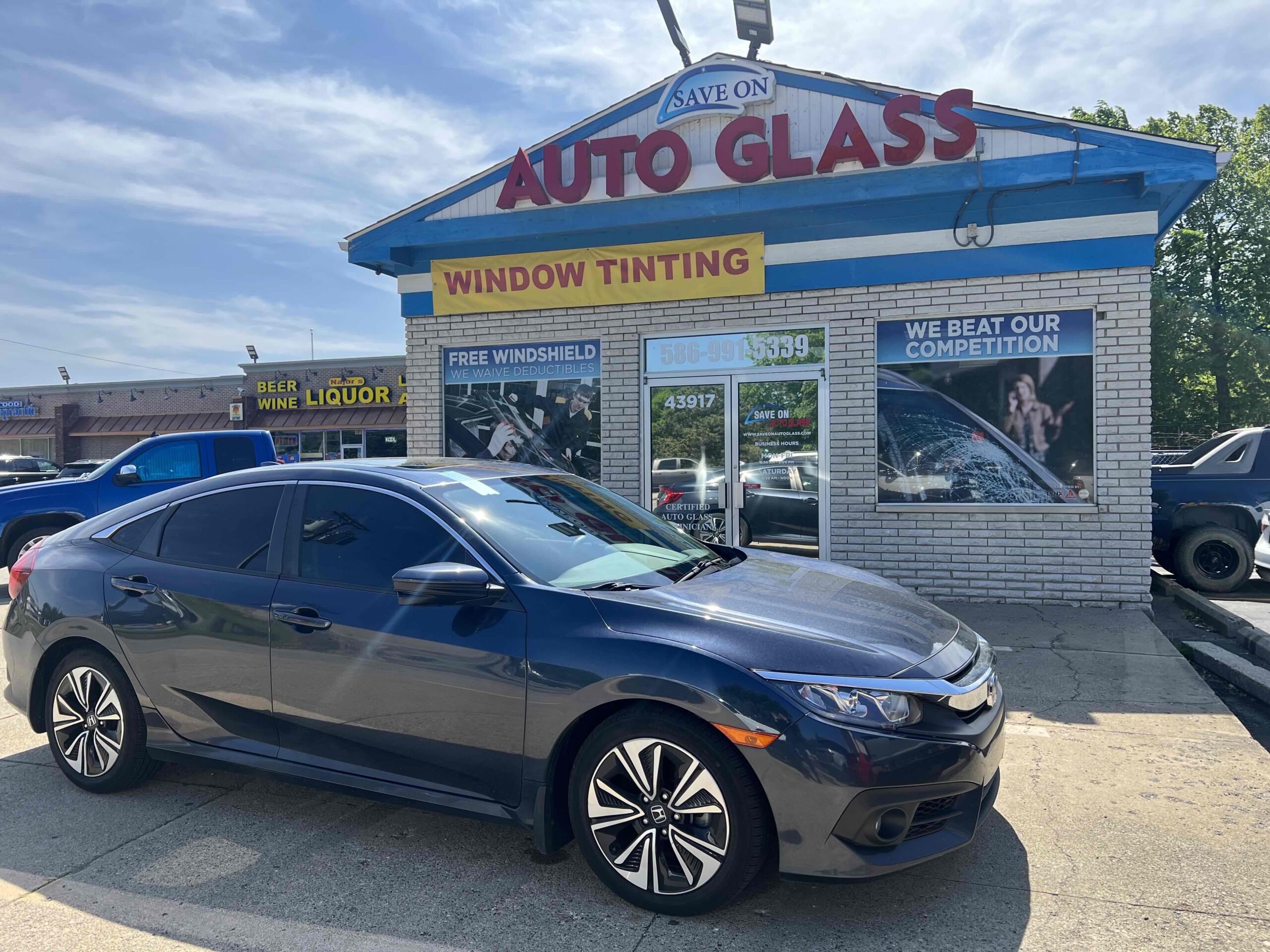 Dark gray car with windshield replaced by Save On Auto Glass, parked in front of the Save On Auto Glass shop
